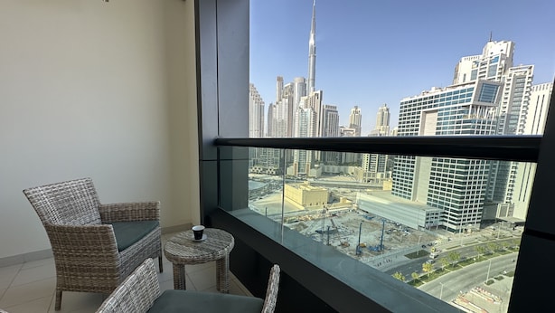 A balcony with wicker furniture and a view of a cityscape including a tall building. - Manzil - Cozy Studio nr Downtown w Canal Views (Dubai)