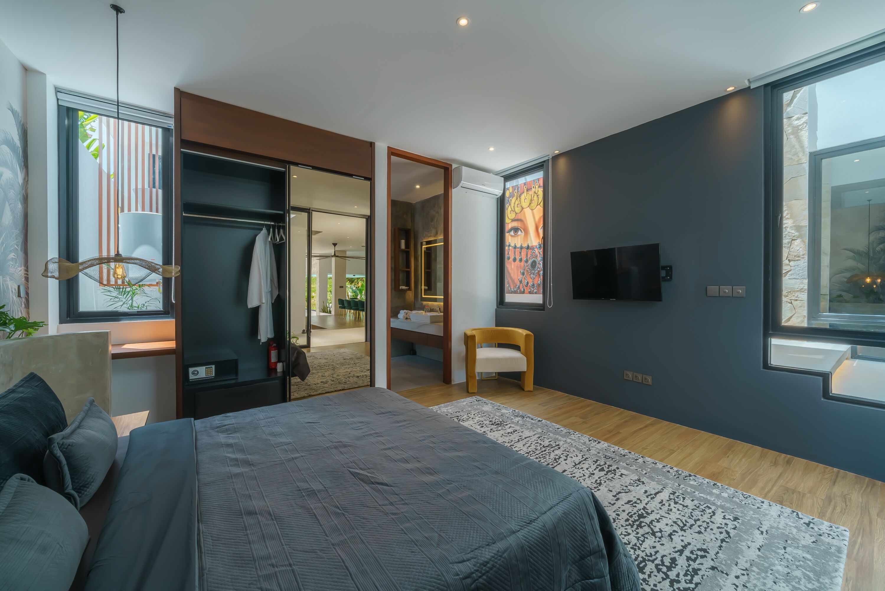 A modern bedroom with a large bed, a walk-in closet, a TV, and a view of the outdoors.