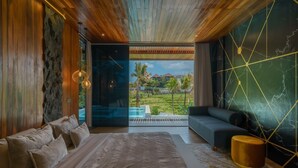 Quarto moderno com cama grande, sofá e vista para uma piscina e vegetação.