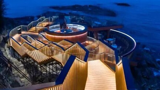 Una terraza de madera que lleva a una estructura circular con una zona de estar central, con vistas a una playa.