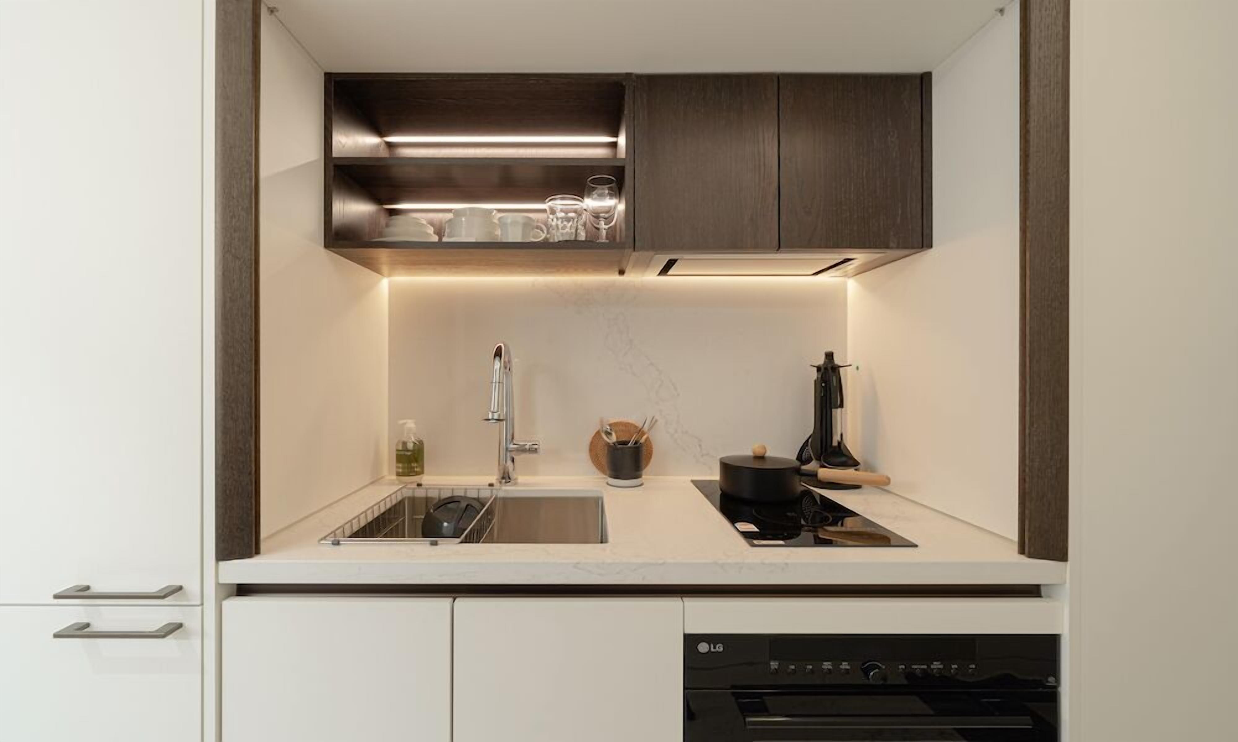 A modern kitchen with a built-in dishwasher, a sink, a stove, and a countertop with a glass of water and a bottle of dish soap.