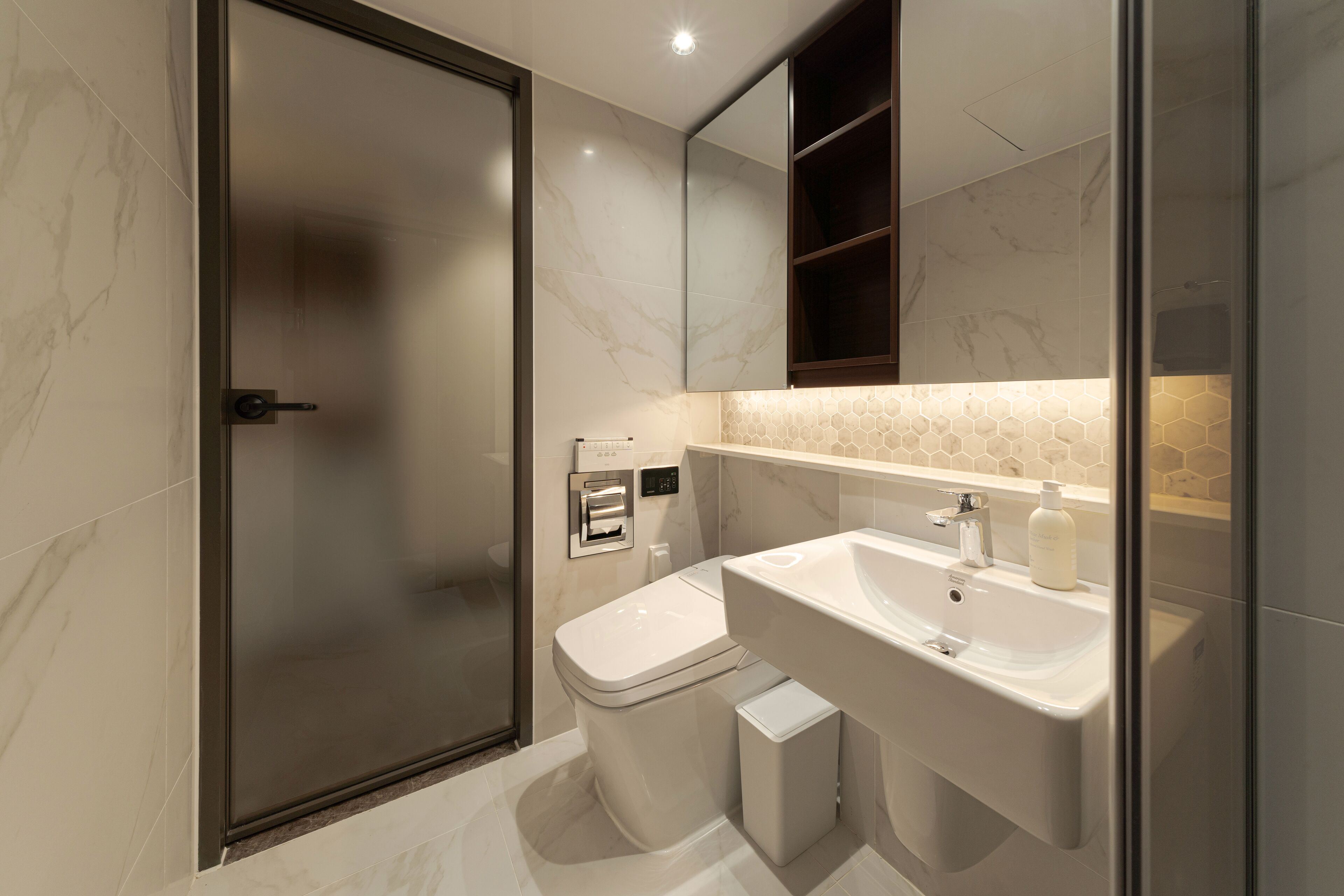 Un baño moderno con cabina de ducha de vidrio, inodoro, lavabo y espejo sobre el lavabo.