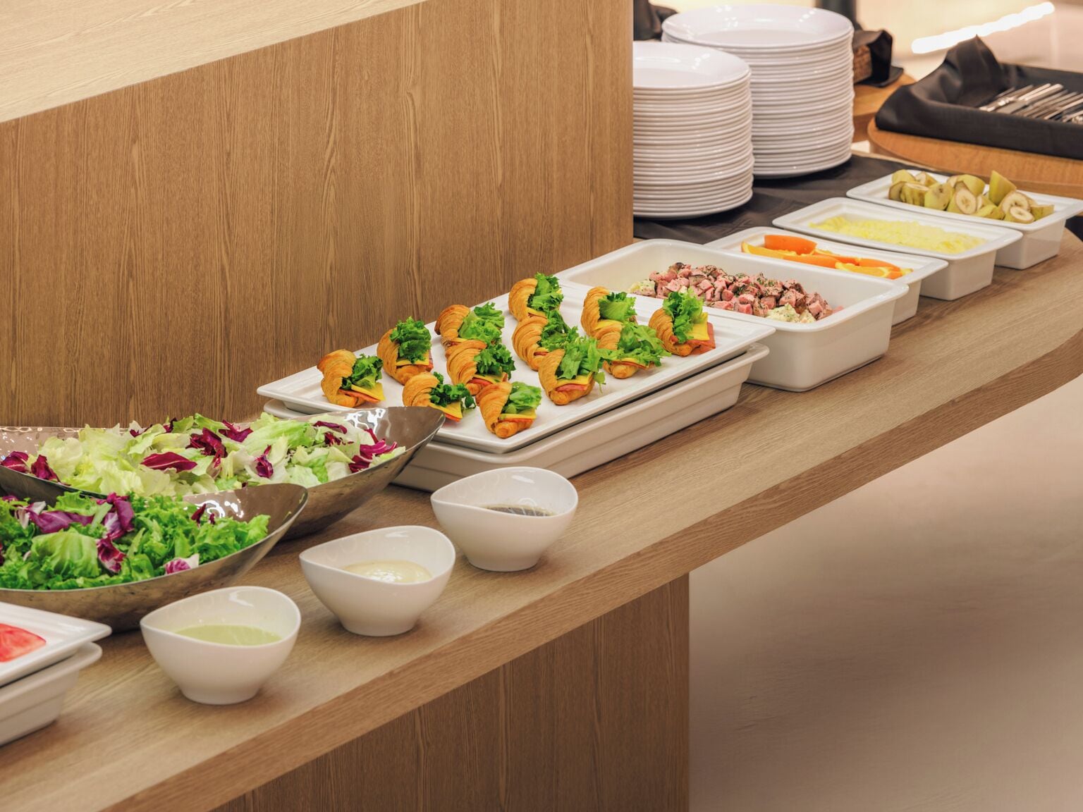 A buffet table with various food items including salads, croissants, and fruit.