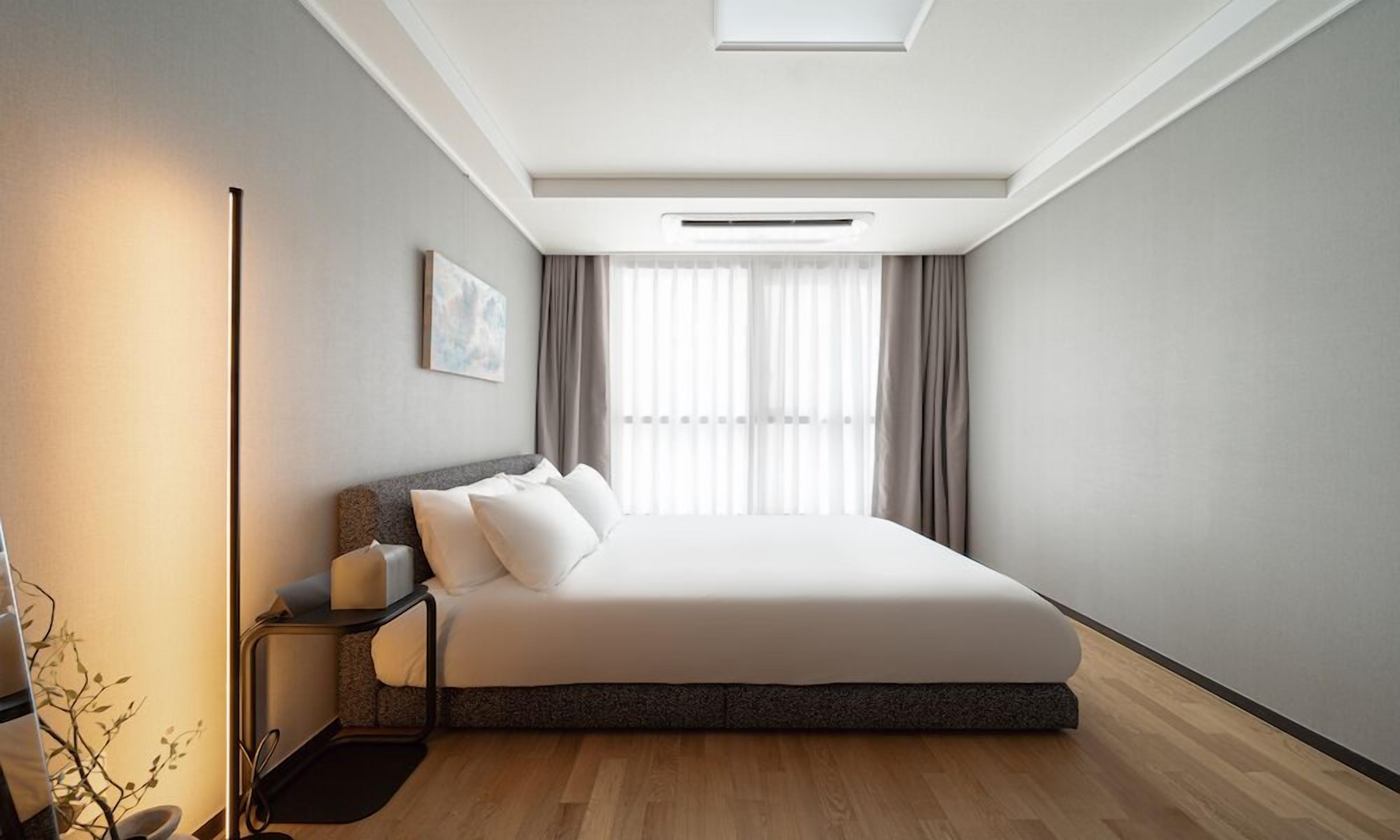 A modern bedroom with a large bed, a bedside table, a floor lamp, and a window with curtains.