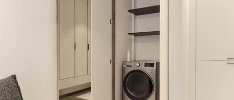 A laundry room with a washing machine, shelves, and a cabinet.