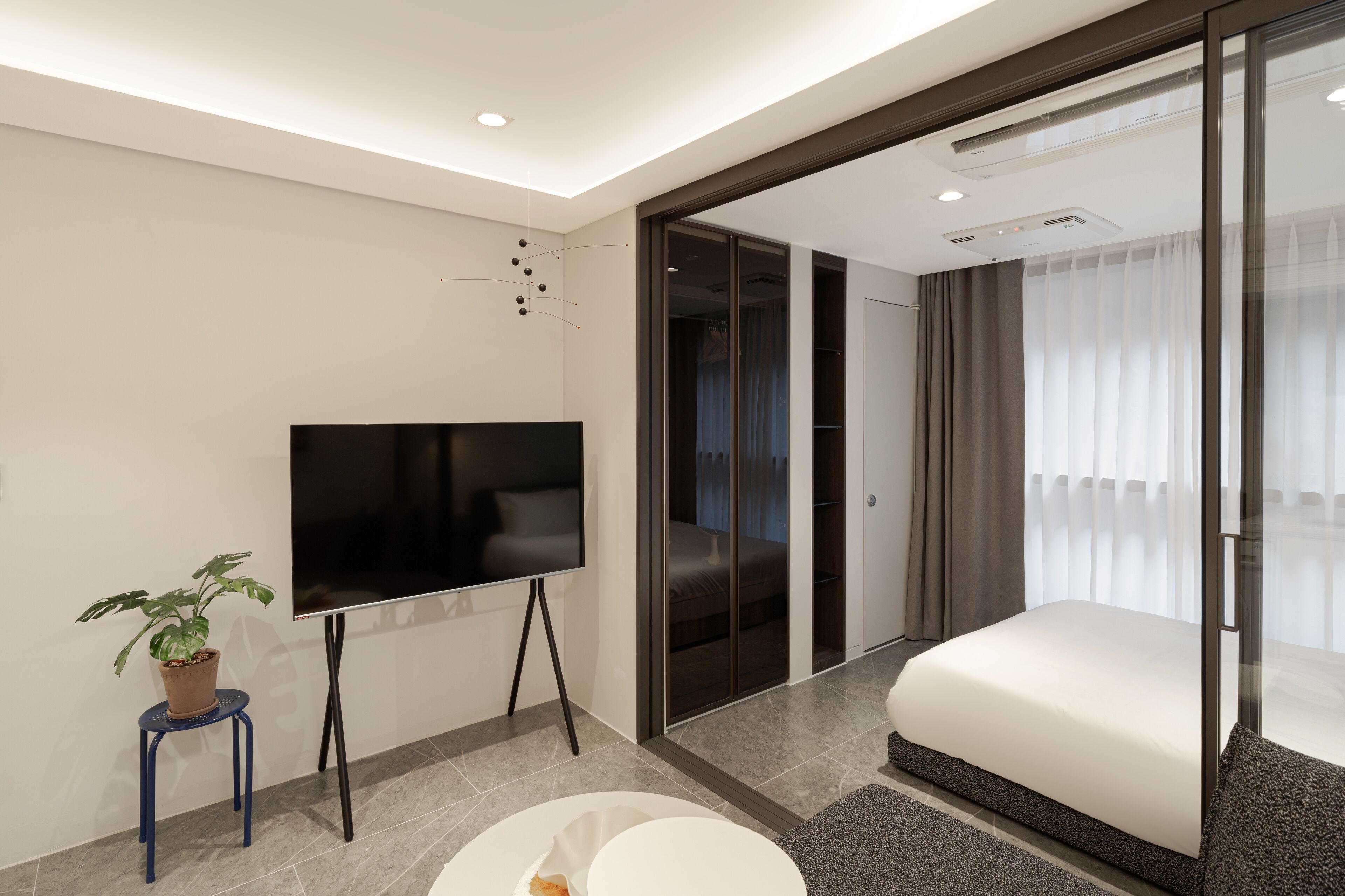 Ein modernes Hotelzimmer mit Fernseher, kleiner Topfpflanze, Bett und Glastür zum Balkon.