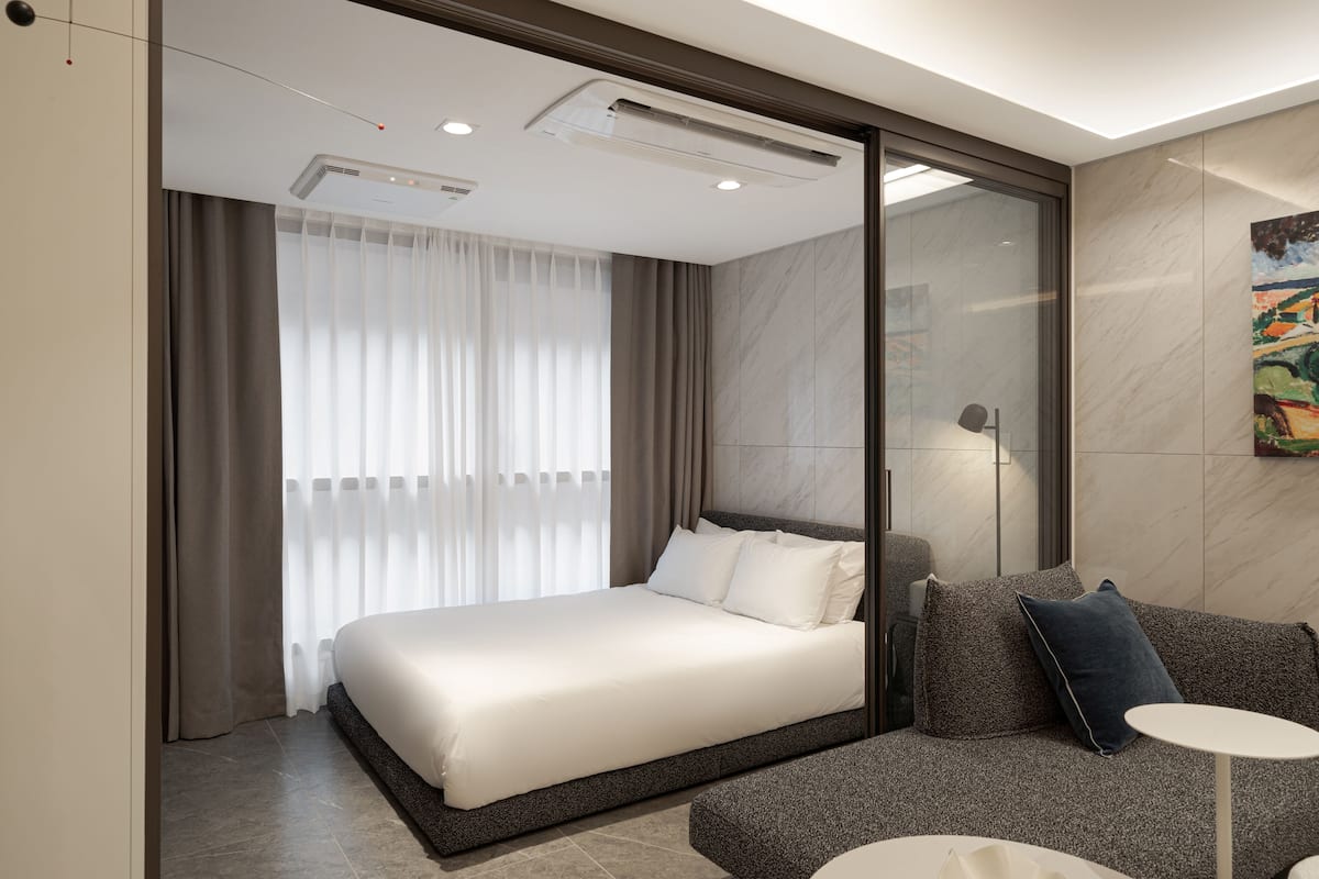 A modern hotel room with a large bed, a sofa, a small table, and a painting on the wall.