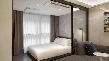 Una habitación de hotel moderna con una cama grande, un sofá, una mesita y un cuadro en la pared.