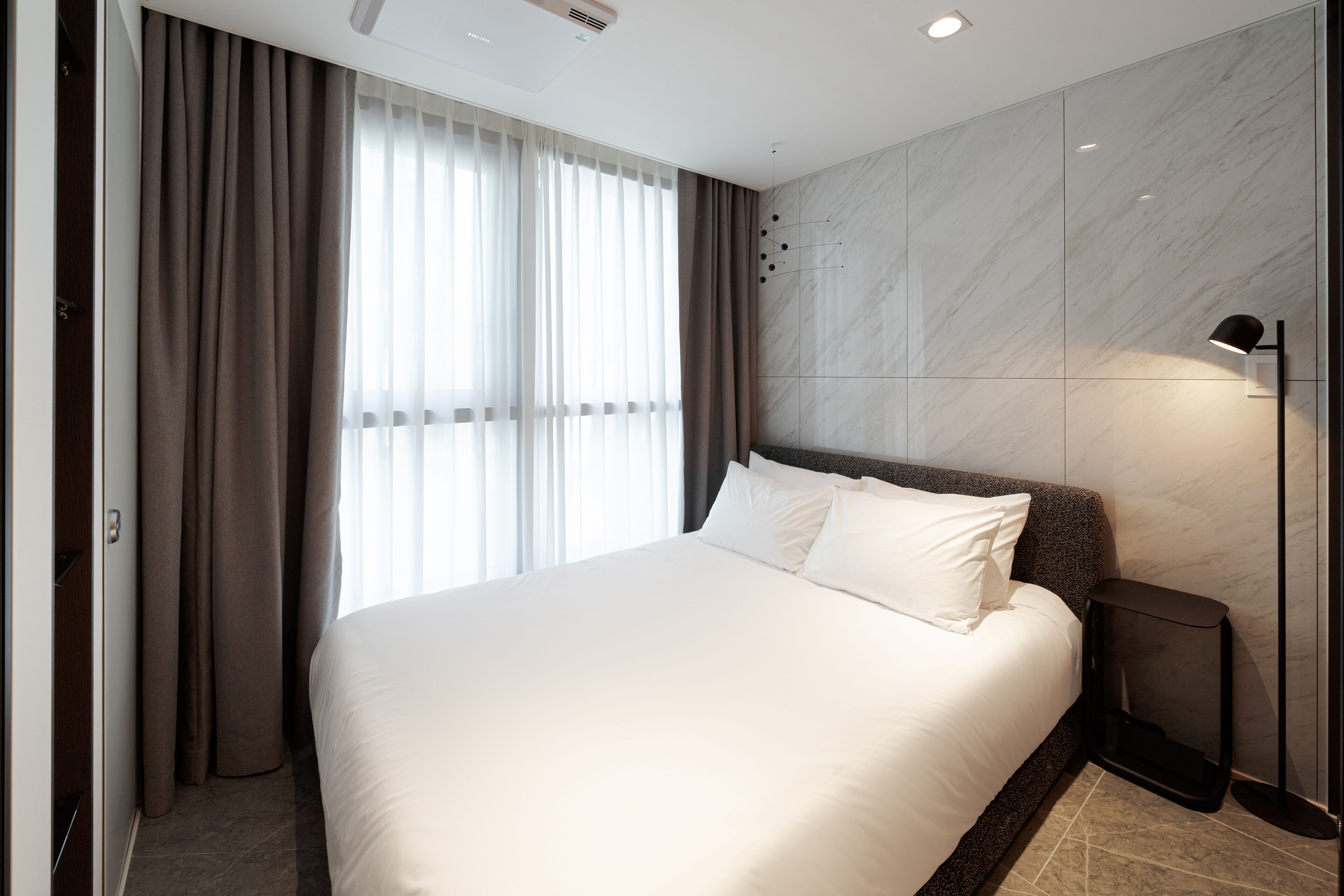 A modern hotel room with a large bed, a nightstand, and a wall-mounted lamp.