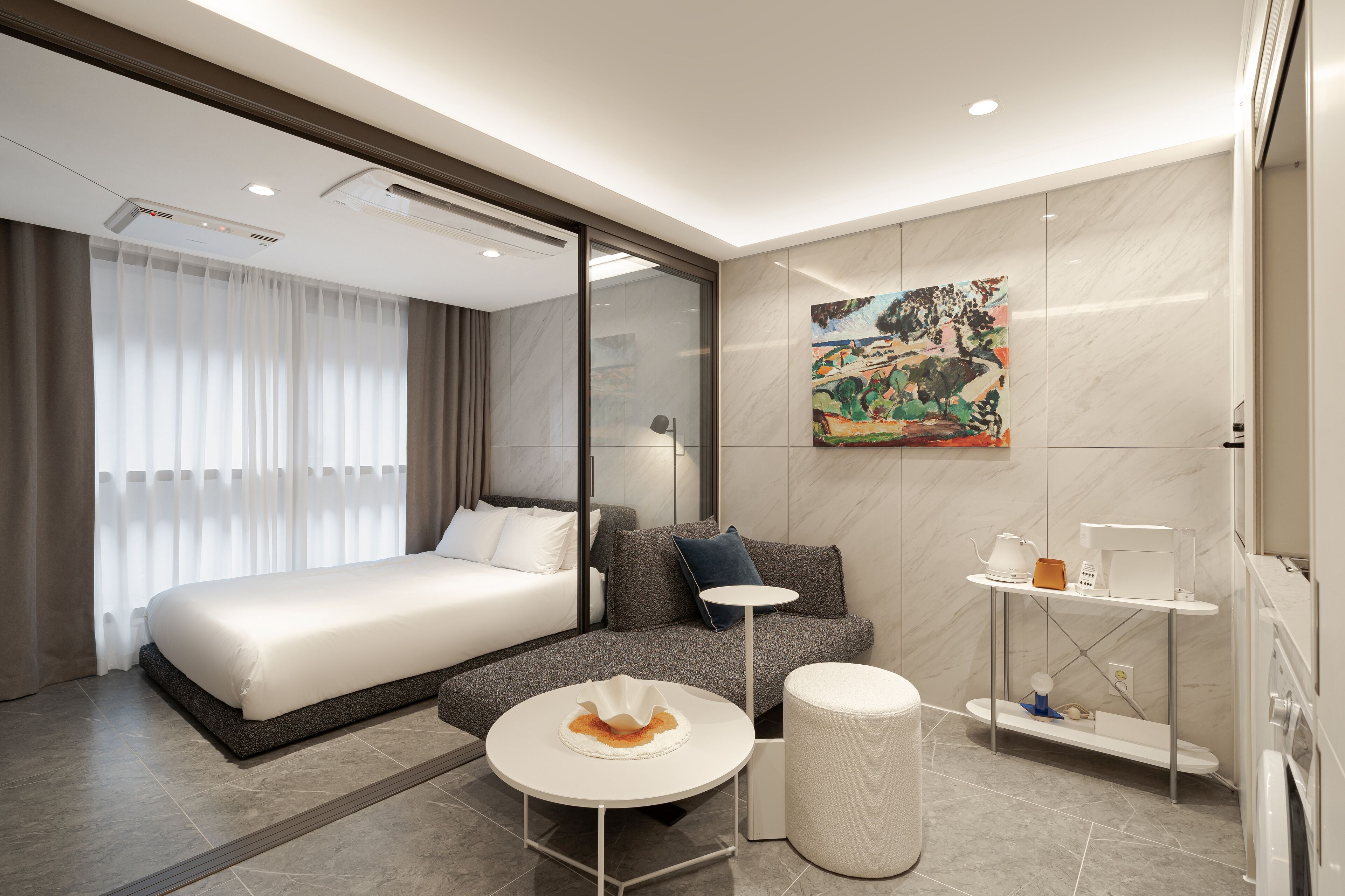 A modern hotel room with a large bed, a sofa, a small table, and a bathroom area.