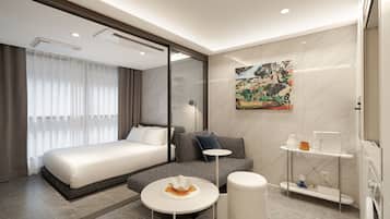 A modern hotel room with a large bed, a sofa, a small table, and a bathroom area.