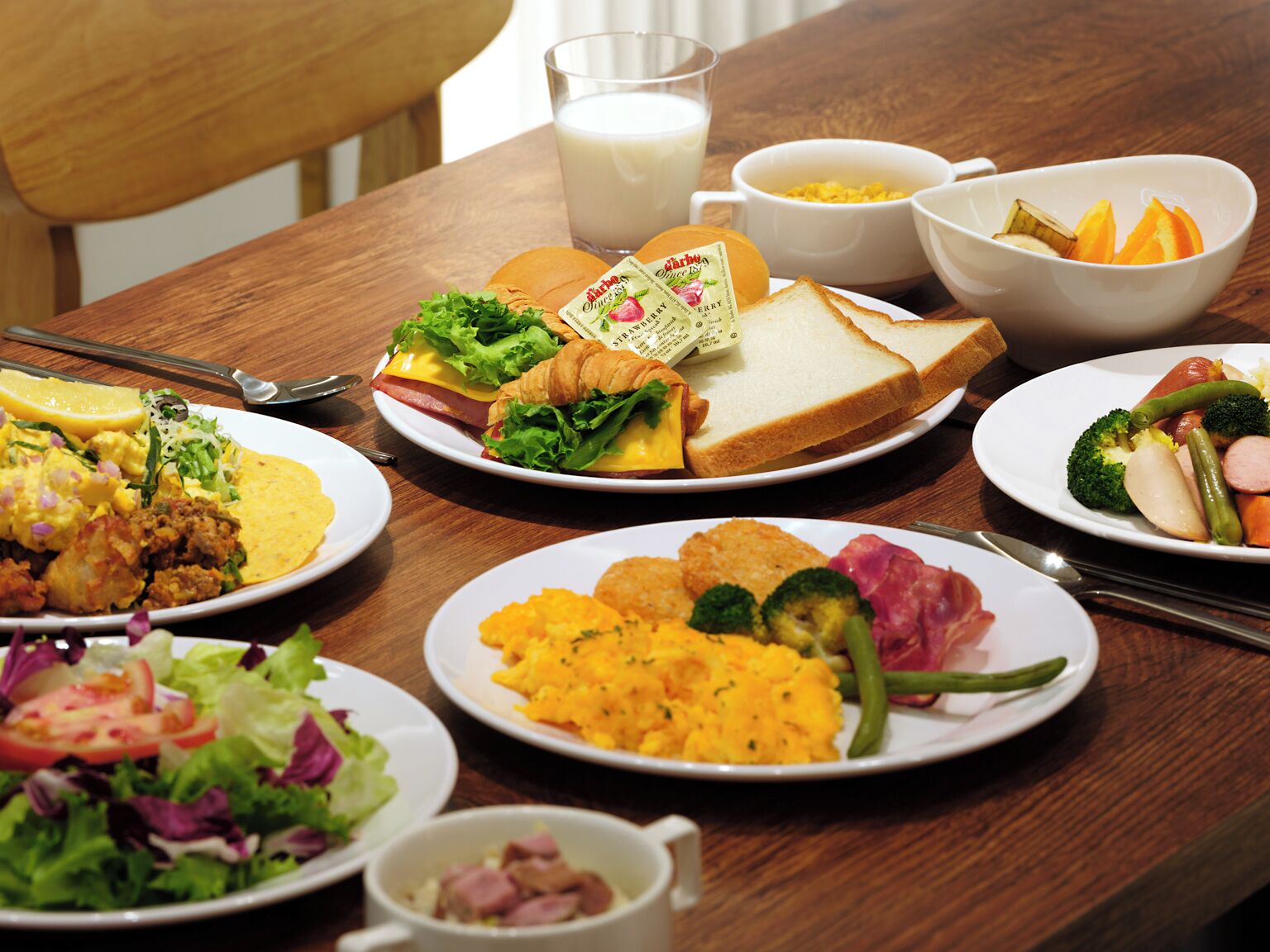 A dining table with various plates of food, including sandwiches, salads, and a glass of milk.