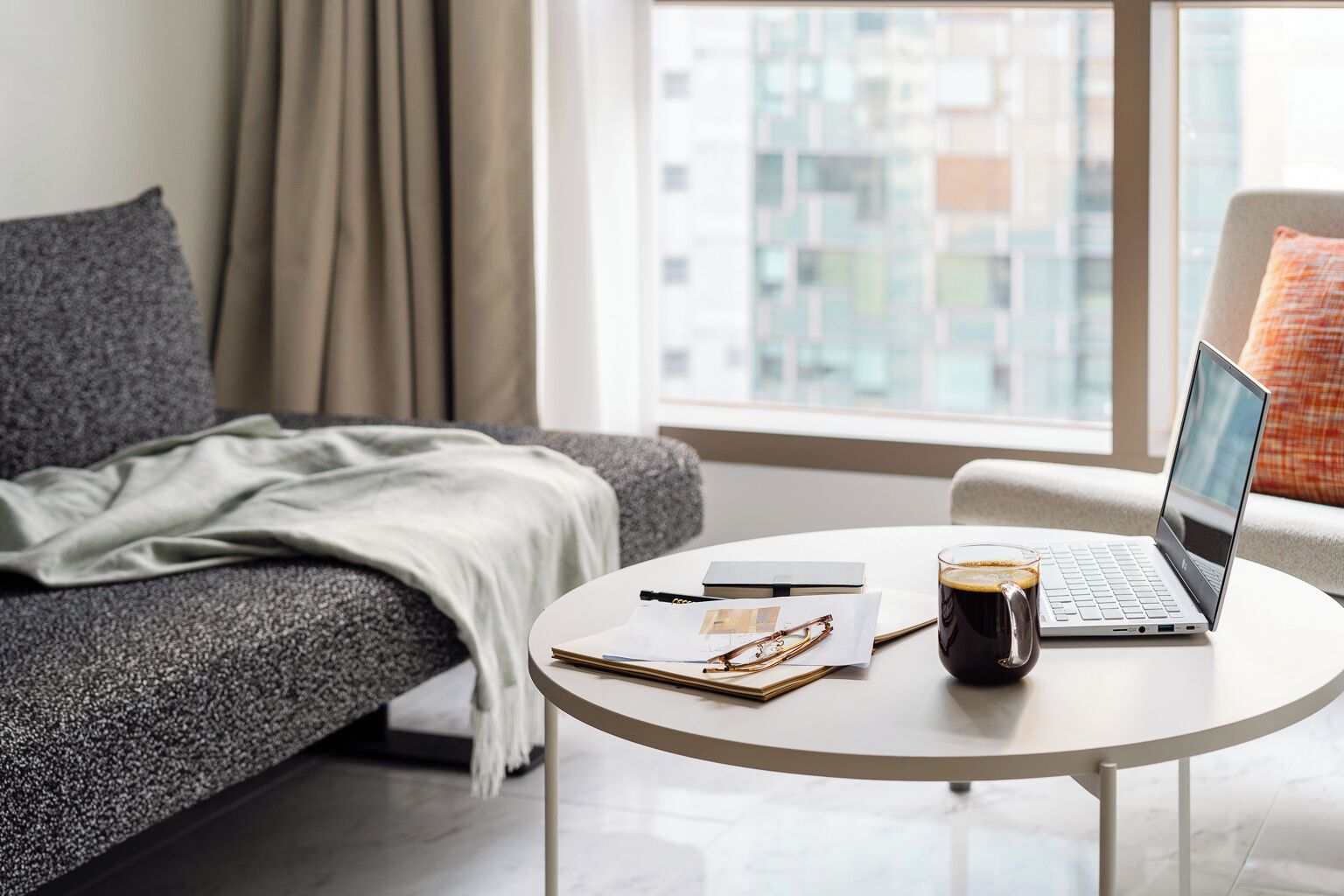 Een moderne woonkamer met een grijze bank, een ronde salontafel en een laptop.