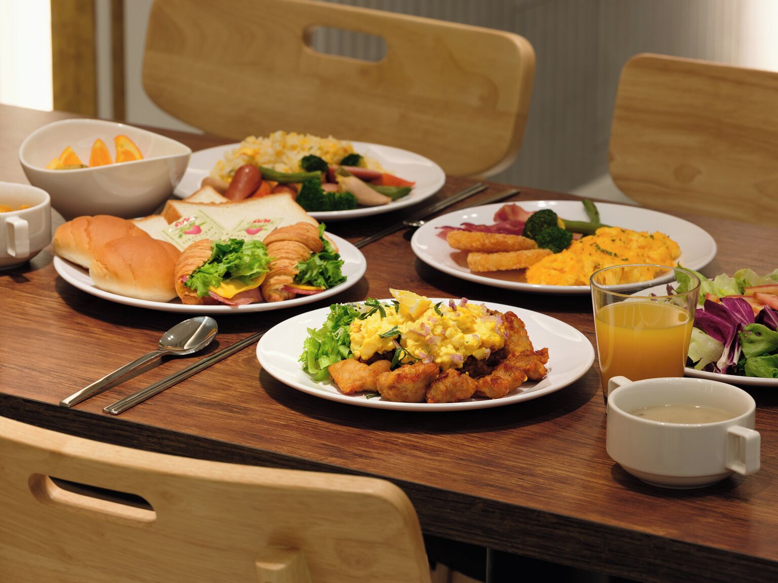 Uma mesa de jantar com vários pratos de comida, incluindo sanduíches, saladas e um copo de suco de laranja.