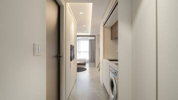 A modern, narrow hallway with a washing machine, a kitchen area, and a living space visible in the distance.