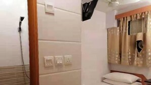 Une chambre d’hôtel de taille réduite, comprenant un lit simple, une petite table de chevet, une prise de courant et une fenêtre avec des rideaux.