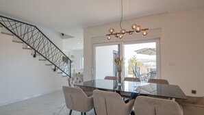 Un comedor moderno con una mesa de vidrio, sillas color beige y una escalera con barandilla metálica.