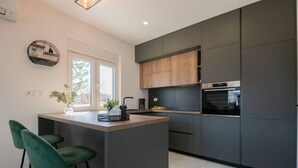 Una cocina moderna con una isla central, armarios oscuros y un ventanal que aporta luz natural.