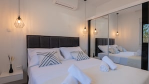 Un dormitorio moderno con una cama grande, ropa de cama blanca y almohadas estampadas en blanco y negro. Hay dos mesitas de noche, una con un jarrón y otra con una lámpara.
