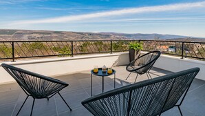Una terraza con dos sillas de mimbre negro y una pequeña mesa redonda con bebidas, con vistas a un paisaje pintoresco.