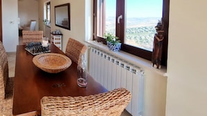 Un comedor con una mesa de madera, sillas de mimbre, un tablero de ajedrez y vistas al paisaje a través de una ventana.