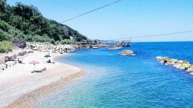 Una playa con agua cristalina, una persona en el agua y un puente distante.