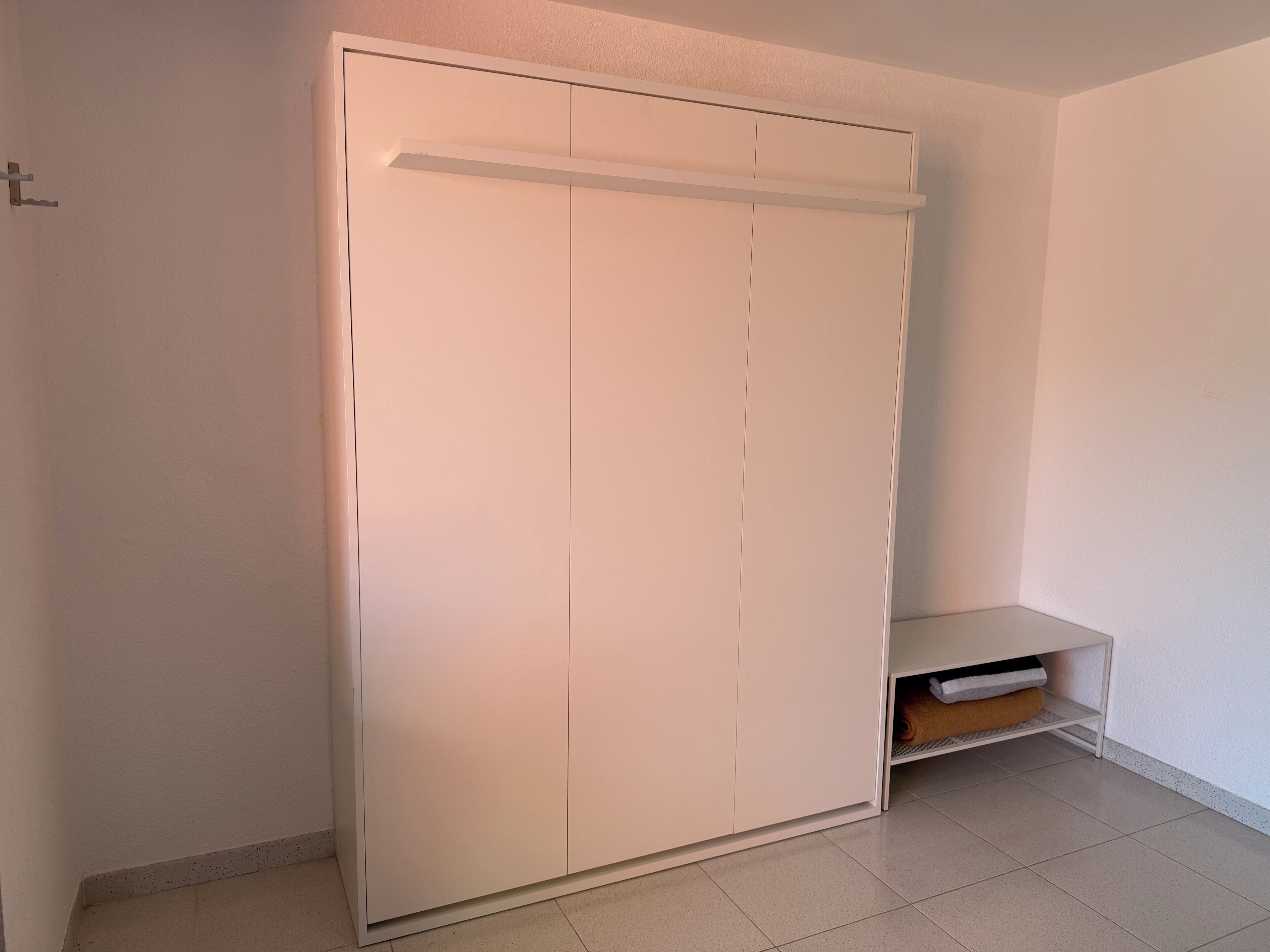 Een witte kast met een schuifdeur en een plank eronder.