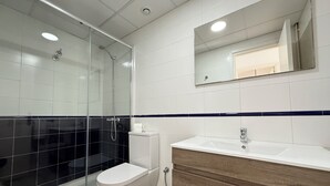 Et moderne badeværelse med brusekabine i glas, toilet, vask med spejl og en trækommode.