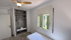 Una habitación con cama, armario, ventilador de techo y ventana con vistas.