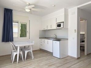 Une cuisine de taille réduite, avec des meubles blancs, un four à micro-ondes, un évier et un ventilateur de plafond.