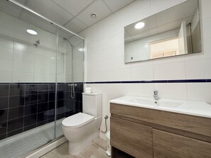 A modern bathroom with a glass shower enclosure, a toilet, a sink with a mirror, and a wooden vanity.