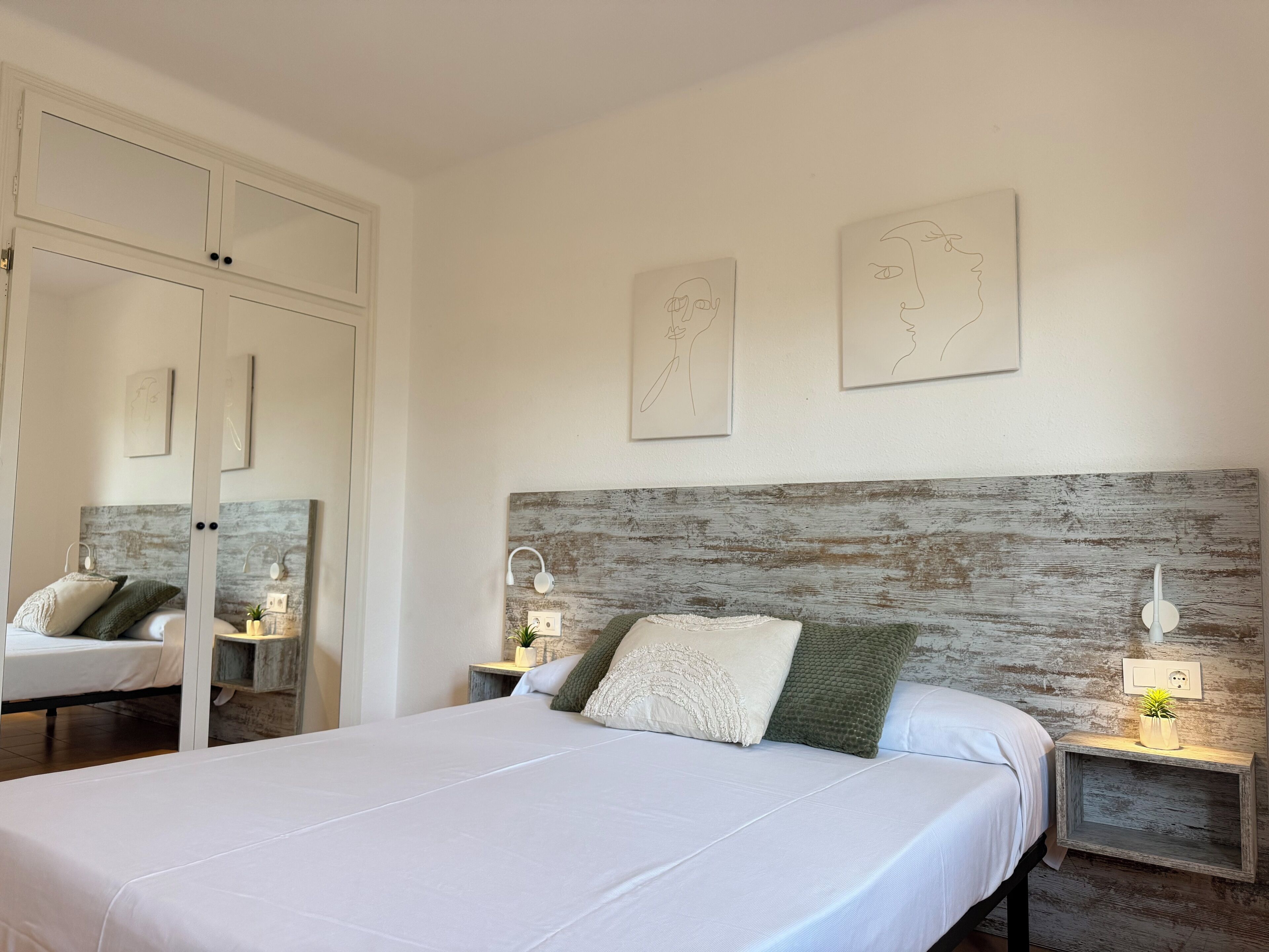 Une chambre à coucher avec un grand lit, deux tables de chevet avec des lampes, une tête de lit en bois et deux œuvres d’art accrochées au mur.