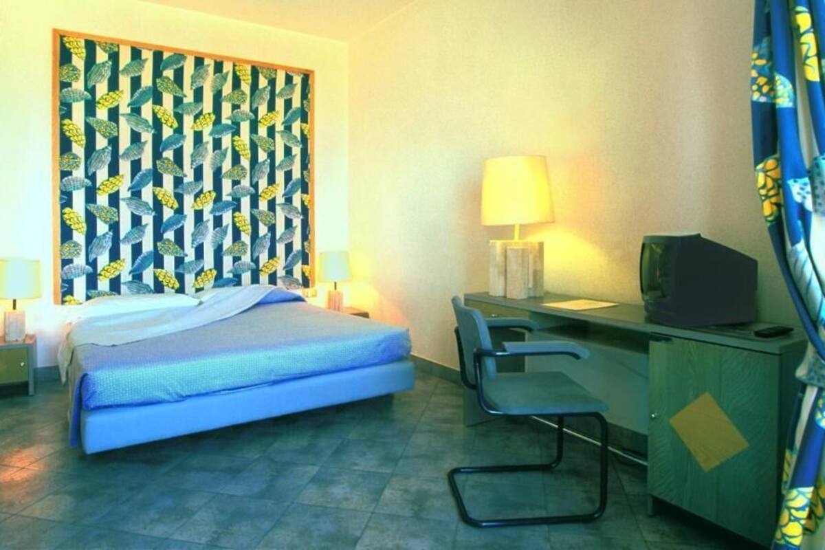A hotel room with a bed, a desk with a lamp, a chair, a television, and curtains.