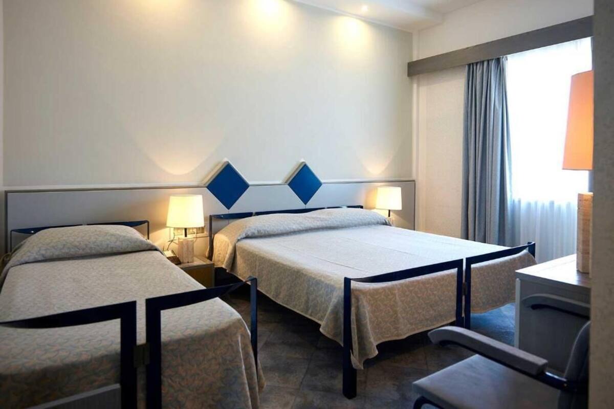 A hotel room with two single beds, a desk, and a chair.