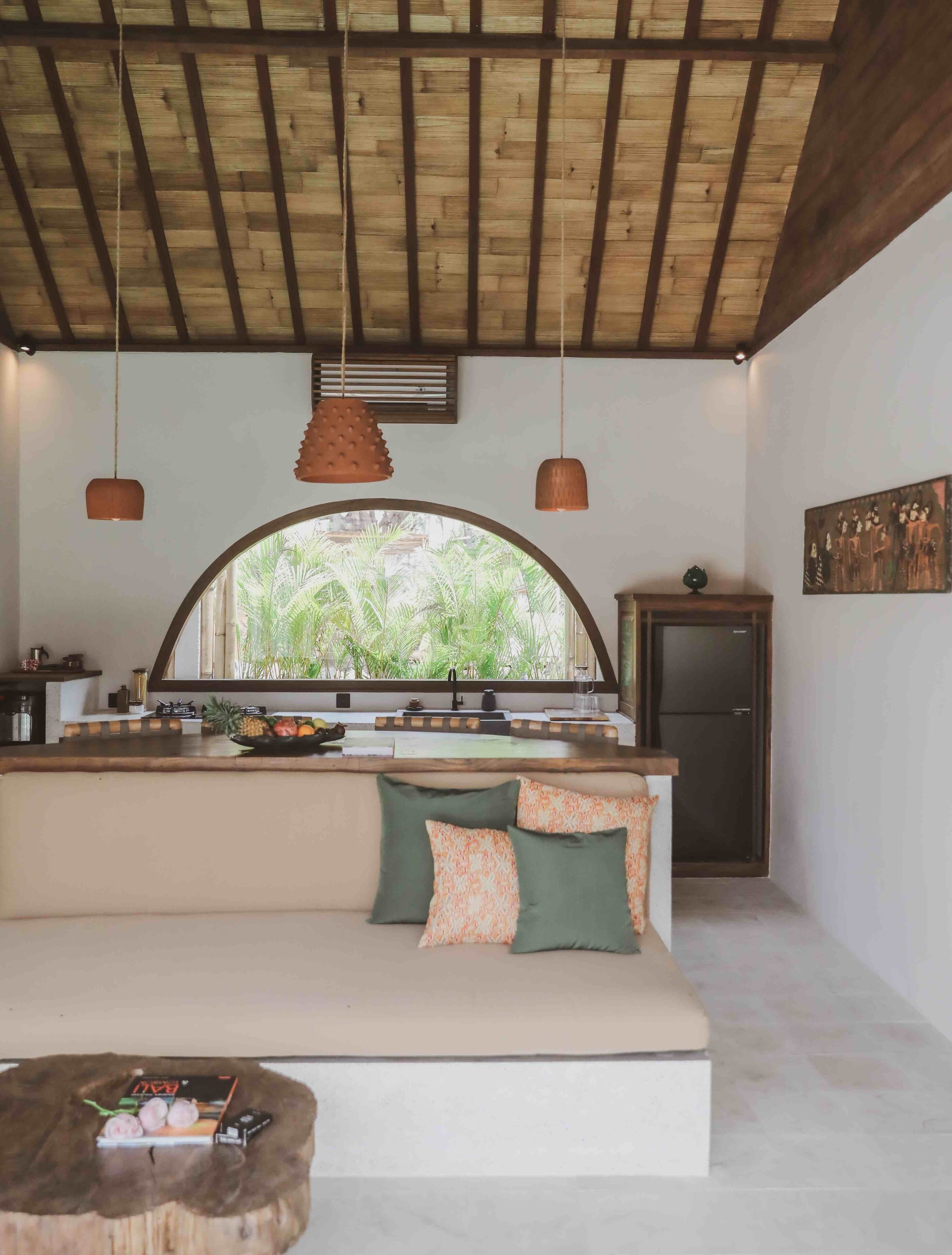 A cozy room with a wooden ceiling, a large window, a sofa, and a small table with a fruit bowl.