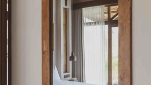 Un dormitorio con techo de madera, cama, mesita de noche y ventana con cortinas.