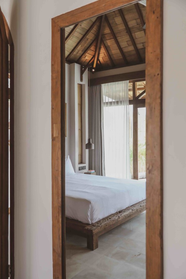 Un dormitorio con techo de madera, cama, mesita de noche y ventana con cortinas.