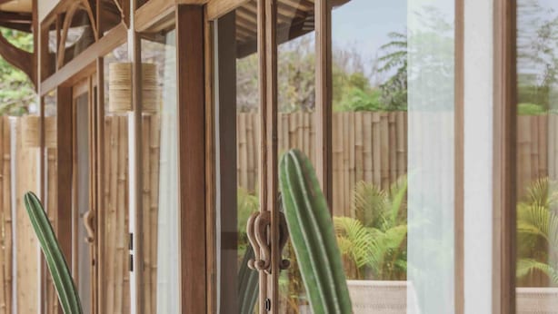 Un espacio al aire libre cubierto con vigas de madera y puertas de vidrio, que incluye dos macetas grandes de terracota con cactus.