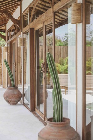 Un espacio al aire libre cubierto con vigas de madera y puertas de vidrio, que incluye dos macetas grandes de terracota con cactus.