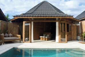 Una estructura de madera con techo de tejas, piscina y un espacio de descanso con cojines.