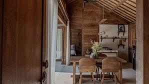 Un interior rústico de madera con comedor que incluye una mesa y sillas de madera, un ventilador de techo y una cocina con estantes de madera.