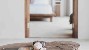 A wooden table with a magazine and a pink rose. A bed with white bedding is in the background.