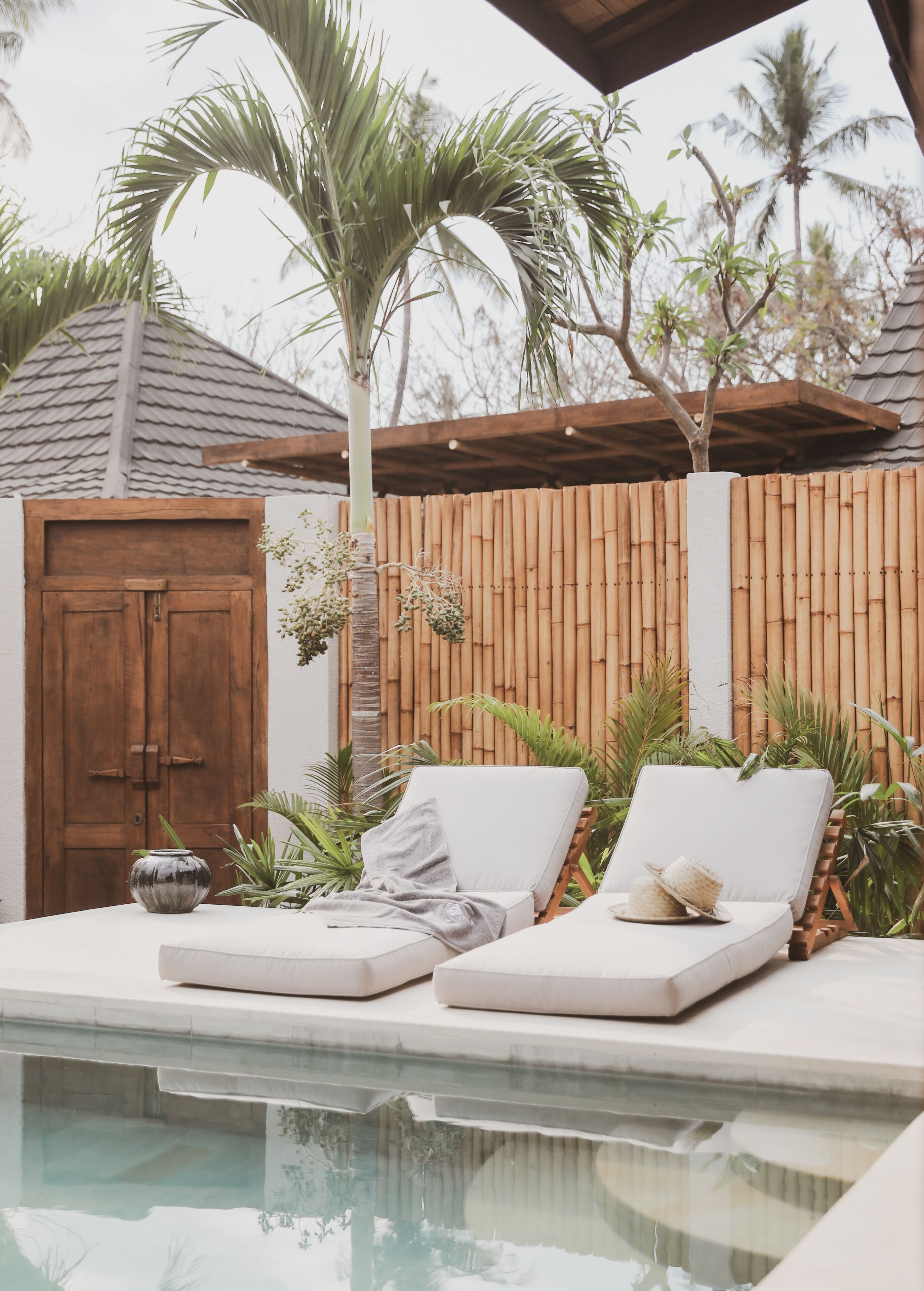 Área de piscina com duas espreguiçadeiras, uma porta de madeira e um cercado de bambu.