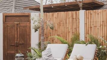 Área de piscina com duas espreguiçadeiras, uma porta de madeira e um cercado de bambu.