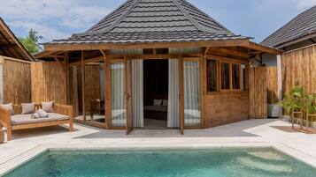 A poolside area with a wooden deck, a covered seating area, and a building with a tiled roof.