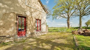 A rustic stone building with two red-framed windows, a grassy yard, and a large tree. - Holiday Home 'Maison De Campagne SPA, Rennes Parc Expo' with Jacuzzi, Private Garden & Wi-Fi (Mordelles)
