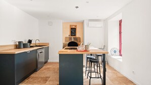 A modern kitchen with a central island, dark cabinetry, and a window with a red door. - Holiday Home 'Maison De Campagne SPA, Rennes Parc Expo' with Jacuzzi, Private Garden & Wi-Fi (Mordelles)