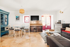 Ein Wohnzimmer mit Fernseher, Klavier, Esstisch mit Stühlen, einer Couch und einem Schrank.