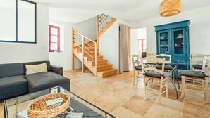 A living room with a sofa, coffee table, wicker basket, and a staircase leading to another room. - Holiday Home 'Maison De Campagne SPA, Rennes Parc Expo' with Jacuzzi, Private Garden & Wi-Fi (Mordelles)