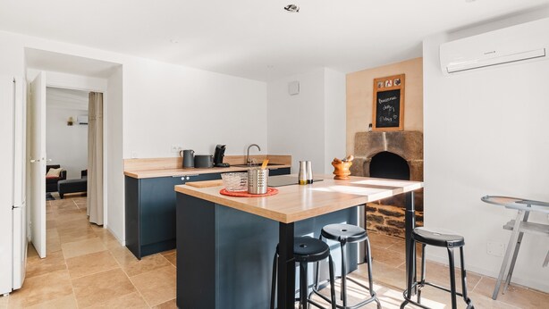 A modern kitchen with a central island, a stone fireplace, and a bar area. - Holiday Home 'Maison De Campagne SPA, Rennes Parc Expo' with Jacuzzi, Private Garden & Wi-Fi (Mordelles)